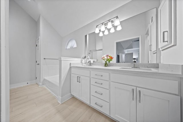 bathroom featuring double vanity, a garden tub, vaulted ceiling, wood finished floors, and a sink