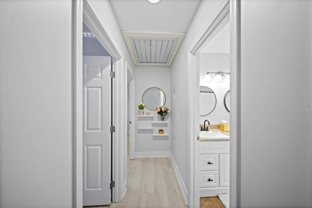 hall with baseboards, a sink, and light wood-style flooring