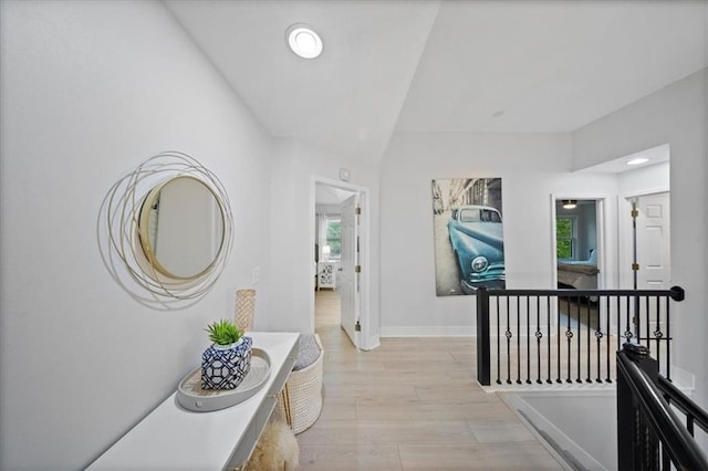 hallway with light wood-type flooring, baseboards, lofted ceiling, and an upstairs landing