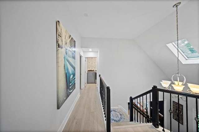 hallway featuring baseboards, wood finished floors, vaulted ceiling with skylight, and an upstairs landing