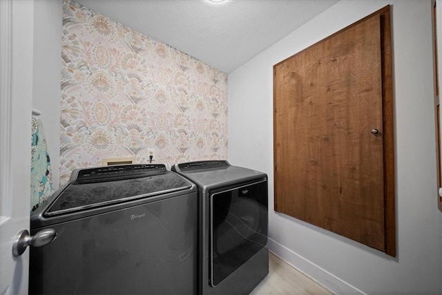 laundry area with laundry area, light wood-style floors, a textured ceiling, baseboards, and washing machine and dryer