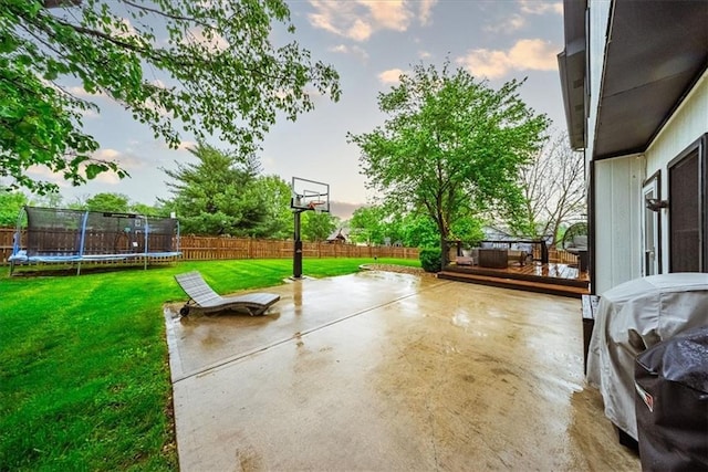 view of basketball court with a fenced backyard, a trampoline, and a yard
