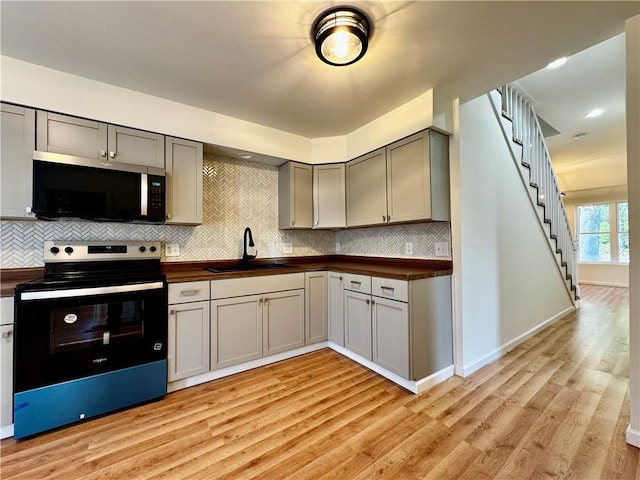 1502 6th Ave, Saint Joseph, MO 64505 - kitchen with decorative backsplash, stainless steel microwave, black electric range, a sink, and light wood-style flooring