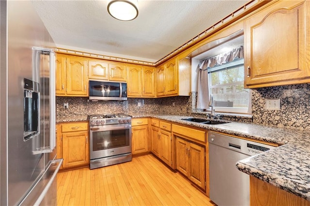 kitchen with appliances with stainless steel finishes, tasteful backsplash, a sink, and light wood-style floors