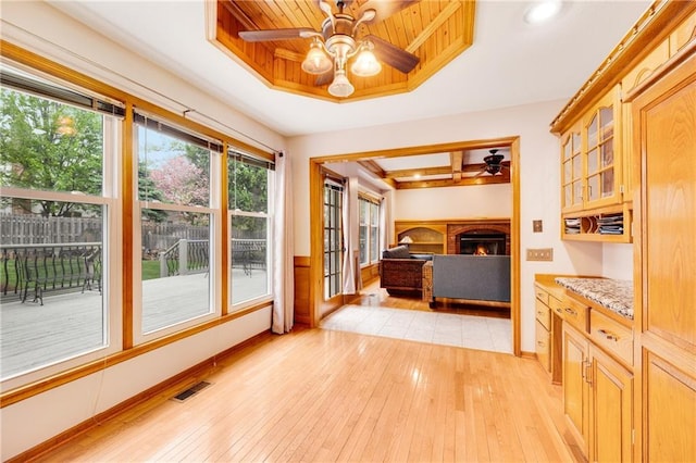 interior space with a brick fireplace, ceiling fan, visible vents, and light wood-type flooring