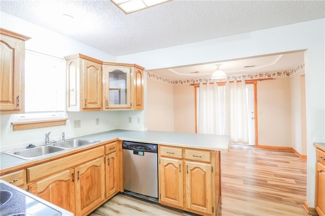 kitchen featuring stainless steel dishwasher, light countertops, a sink, light wood-type flooring, and a peninsula