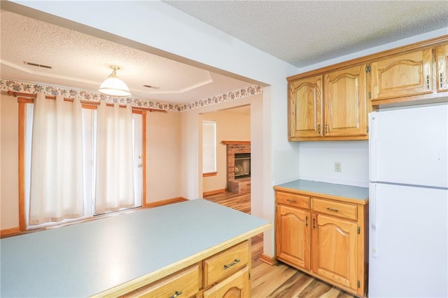 kitchen featuring light wood-style floors, a brick fireplace, light countertops, a textured ceiling, and freestanding refrigerator