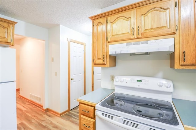 kitchen featuring a textured ceiling, visible vents, under cabinet range hood, light wood-type flooring, and white appliances