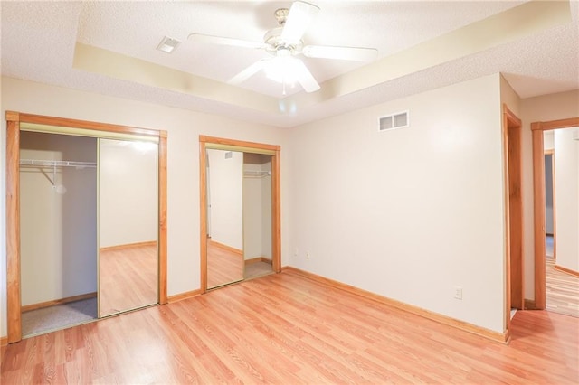 unfurnished bedroom featuring a raised ceiling, visible vents, two closets, and light wood-style flooring