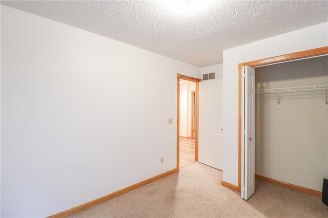 unfurnished bedroom featuring a textured ceiling, carpet flooring, visible vents, baseboards, and a closet