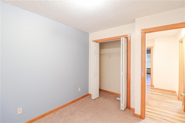 unfurnished bedroom featuring a closet, a textured ceiling, light colored carpet, and baseboards