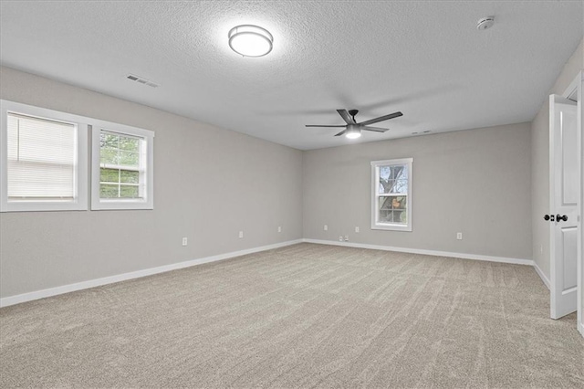 spare room featuring visible vents, baseboards, ceiling fan, light colored carpet, and a textured ceiling