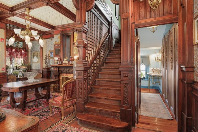 stairway with beam ceiling, an inviting chandelier, ornamental molding, and wood finished floors