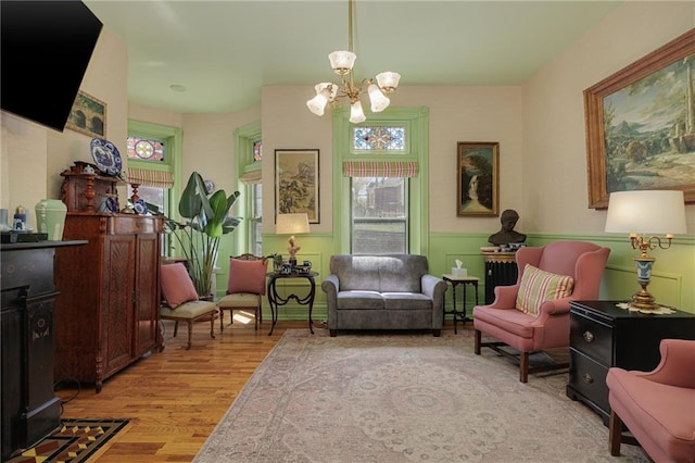 living area with a chandelier, light wood finished floors, and a wainscoted wall