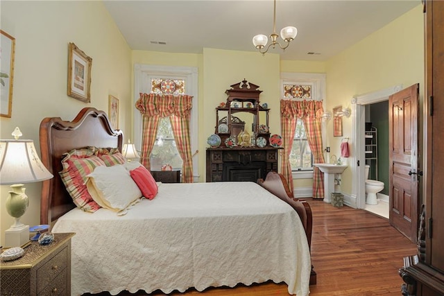 bedroom with an inviting chandelier, ensuite bath, dark wood finished floors, baseboards, and visible vents