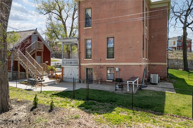 rear view of property featuring fence, brick siding, central AC unit, a patio area, and a lawn