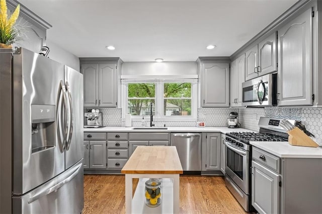 kitchen featuring gray cabinetry, decorative backsplash, stainless steel appliances, and a sink
