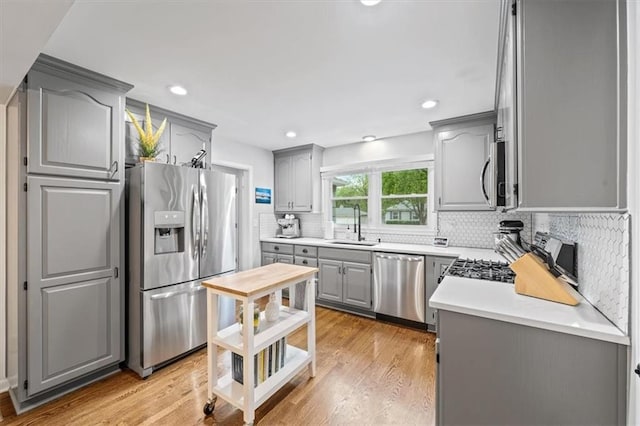 kitchen featuring gray cabinetry, appliances with stainless steel finishes, backsplash, and light wood-style flooring