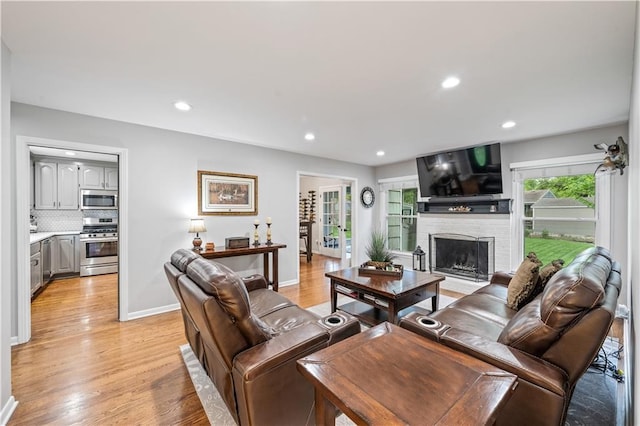 living room featuring recessed lighting, light wood-style flooring, a brick fireplace, and baseboards