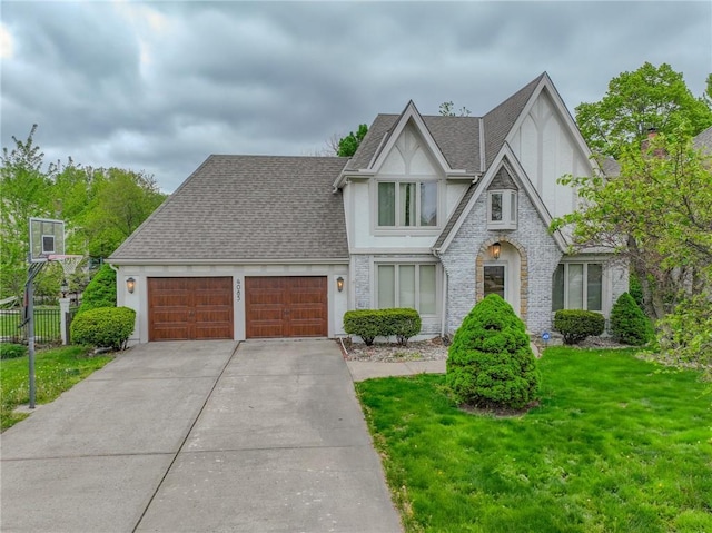 tudor house with stucco siding, a shingled roof, a front lawn, concrete driveway, and an attached garage