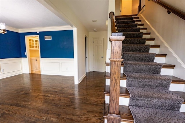 staircase featuring crown molding, visible vents, a decorative wall, wood finished floors, and wainscoting