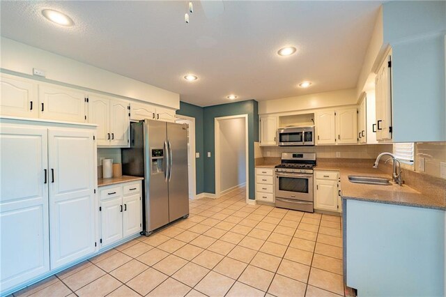 kitchen featuring a sink, light tile patterned floors, backsplash, white cabinetry, and appliances with stainless steel finishes