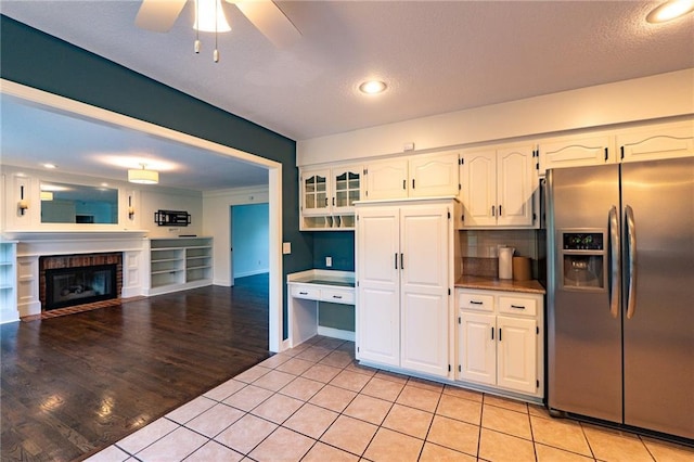 kitchen featuring white cabinetry, ceiling fan, light tile patterned flooring, a fireplace, and stainless steel fridge
