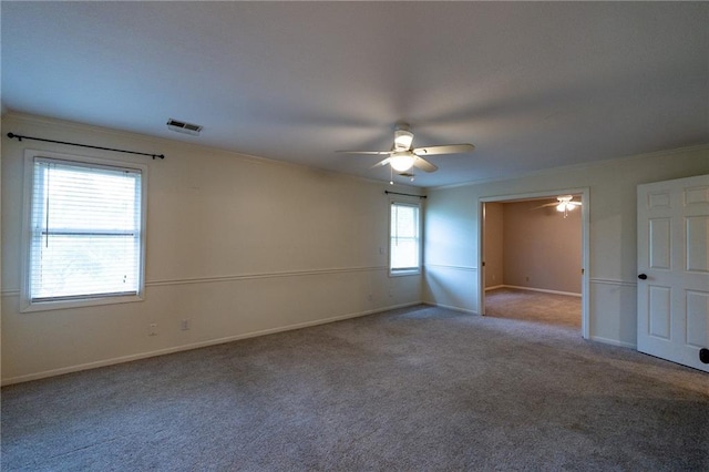 carpeted empty room with baseboards, visible vents, a ceiling fan, and crown molding