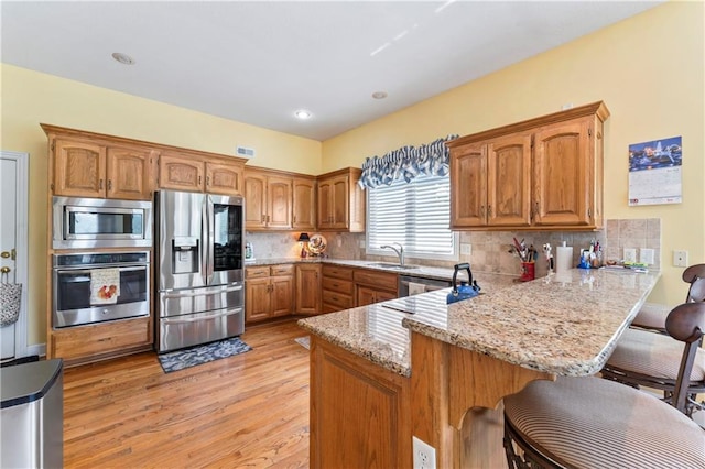 9800 W 147th St, Overland Park, KS 66221 - kitchen with stainless steel appliances, a peninsula, a breakfast bar, light wood finished floors, and brown cabinetry