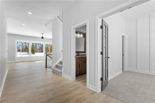 corridor featuring baseboards, light wood finished floors, recessed lighting, and stairs