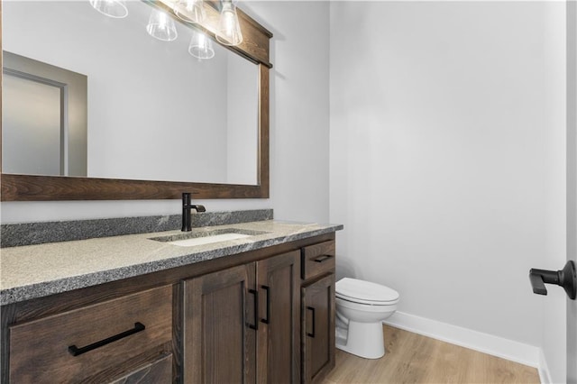 half bath featuring wood finished floors, toilet, vanity, and baseboards