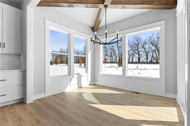 unfurnished dining area featuring a chandelier, light wood-type flooring, beamed ceiling, and baseboards
