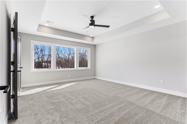 carpeted spare room featuring a ceiling fan, baseboards, and a tray ceiling