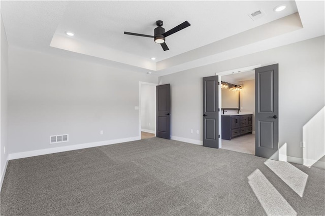 unfurnished bedroom with visible vents, baseboards, light colored carpet, and a tray ceiling