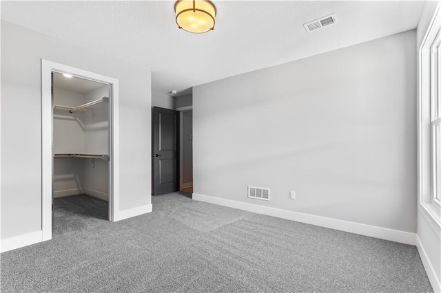 unfurnished bedroom with a walk in closet, visible vents, carpet, and baseboards