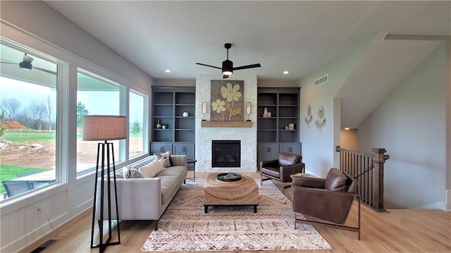 living area with a fireplace, a ceiling fan, visible vents, light wood-style flooring, and baseboards