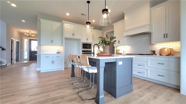 kitchen with tasteful backsplash, appliances with stainless steel finishes, light countertops, light wood-type flooring, and an island with sink
