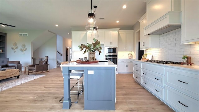 kitchen featuring custom range hood, appliances with stainless steel finishes, visible vents, open floor plan, and a kitchen bar