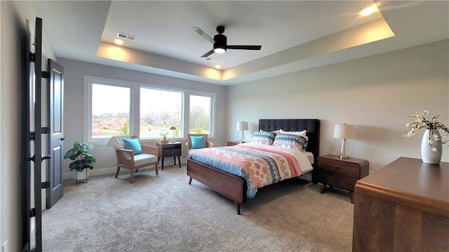 bedroom with visible vents, ceiling fan, a tray ceiling, baseboards, and light carpet