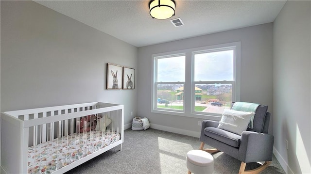 bedroom with carpet floors, a crib, baseboards, visible vents, and a textured ceiling
