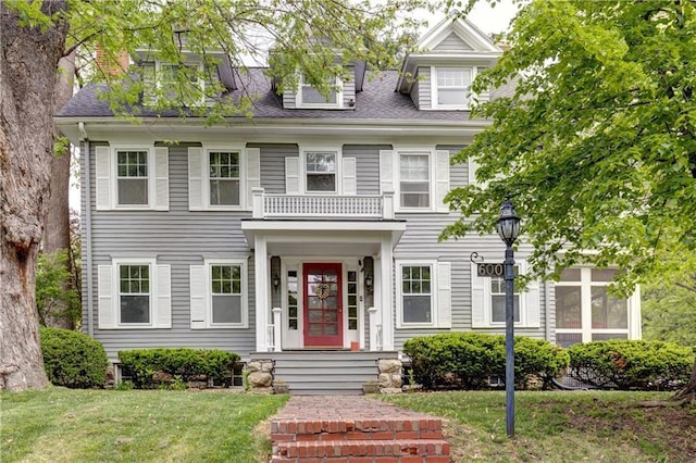 colonial inspired home with a shingled roof, a front lawn, and a balcony
