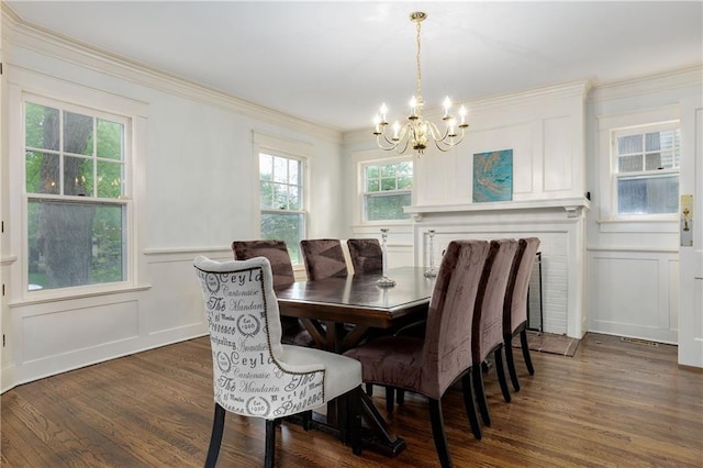 dining area featuring crown molding, a chandelier, a wainscoted wall, dark wood-style floors, and a decorative wall