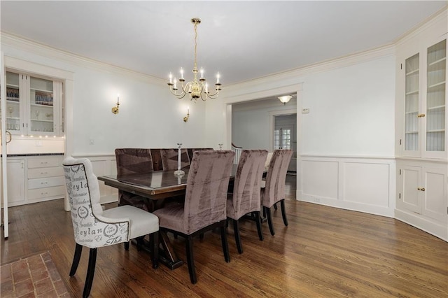 dining space featuring a notable chandelier, a decorative wall, ornamental molding, wainscoting, and dark wood finished floors