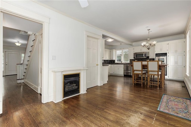 dining area with an inviting chandelier, stairway, a glass covered fireplace, crown molding, and dark wood finished floors