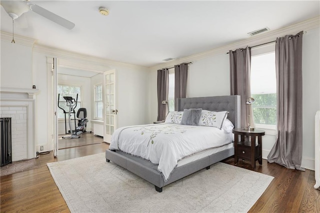 bedroom featuring visible vents, wood finished floors, ornamental molding, and a brick fireplace