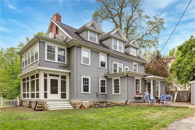rear view of property with fence, a chimney, a lawn, and a sunroom