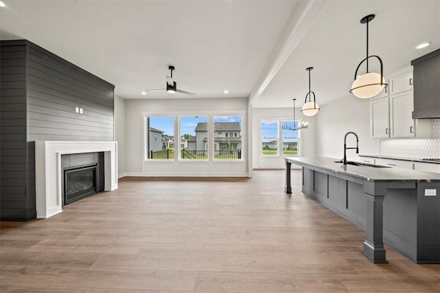 unfurnished living room featuring a ceiling fan, a glass covered fireplace, light wood-type flooring, recessed lighting, and a sink