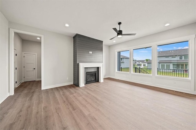 unfurnished living room featuring a glass covered fireplace, baseboards, recessed lighting, a ceiling fan, and light wood finished floors
