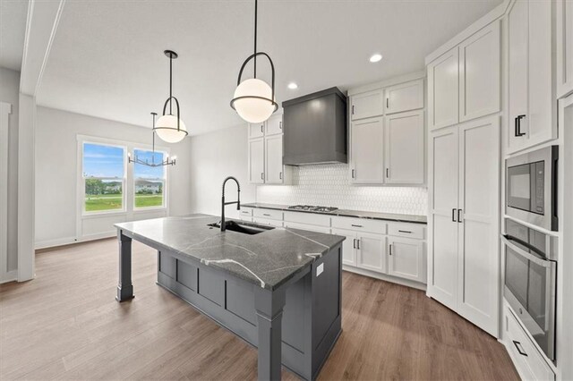 kitchen featuring wood finished floors, wall chimney exhaust hood, tasteful backsplash, a sink, and appliances with stainless steel finishes