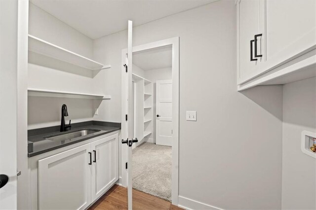 washroom with a sink, washer hookup, cabinet space, and light wood-style flooring